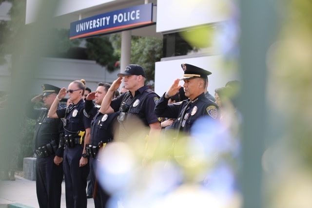 University police officers standing and saluting in front of a building.